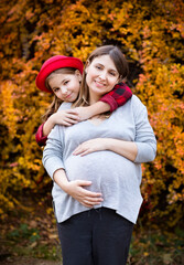 Fototapeta premium Happy young pregnant mother with daughter in autumn park