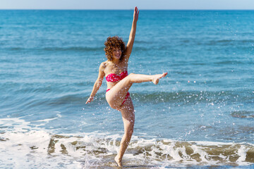 Carefree woman splashing ocean water on beach - 784715432