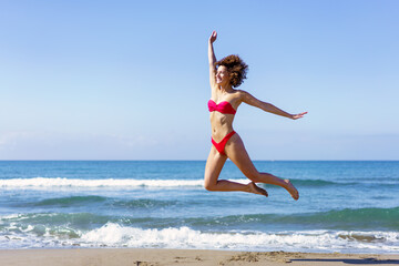 Slim woman in bikini jumping on sandy beach - 784715851
