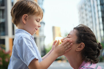 Adorable mother and son smiling happy having fun at city background. Motherhood concept, hugging. Boy 8 years old with mother in bright clothes enjoying summer day. High quality photo