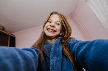 Fototapeta premium A smiling beautiful girl, a cheerful child teenager photographs herself holding a camera, a smartphone, a phone in her hands, showing a grimace on her face, smiling, grimacing. Photography, portrait.