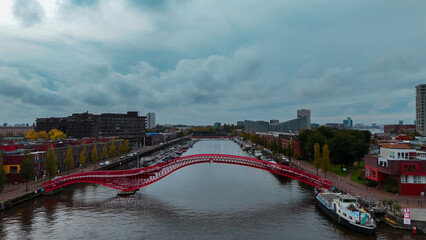 Aerial drone view of modern footbridge Python Bridge at Eastern Docklands neighborhood of Amsterdam Netherlands - obrazy, fototapety, plakaty