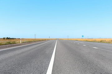 An asphalt road with markings stretches into the distance on a bright summer day. Beautiful road in the steppe.