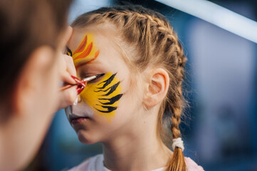 A woman professional artist paints with a brush, a colored pencil on the face of a child, a...