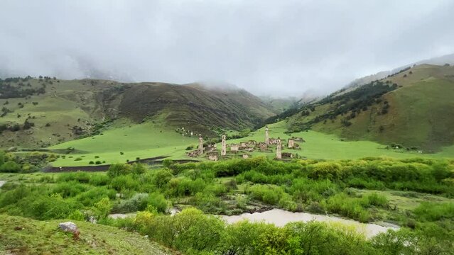 View of the medieval Targim tower complex in the Caucasus mountains surrounded by greenery. The Caucasus Mountains on a cloudy day in Ingushetia. Russia, 4K.