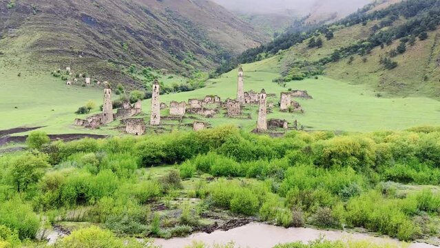 View of the medieval Targim tower complex in the Caucasus mountains surrounded by greenery. The Caucasus Mountains on a cloudy day in Ingushetia. Russia, 4K.