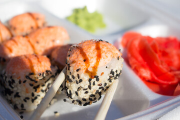Baked sushi rolls with salmon, cheese and sauce on a foamed polystyrene tray.
