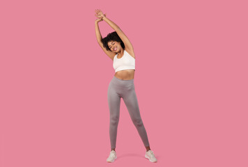 Sporty woman stretching on a pink background