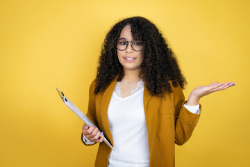 African american business woman with paperwork in hands over yellow background clueless and...