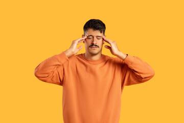 Man with headache holding temples on yellow