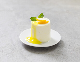 Modern dessert. Lemon cream pudding, Panna Cotta cylindrical shape, with lemon sauce, on a plate. Light grey background. Close-up