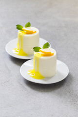 Vegan dessert. Lemon cream pudding cylindrical shape, with lemon sauce, on a plate. Light grey background. Close-up