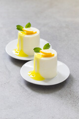 Vegan dessert. Lemon cream pudding cylindrical shape, with lemon sauce, on a plate. Light grey background. Close-up
