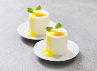 Lemon cream pudding cylindrical shape, with lemon sauce, on a plate. Light grey background. Close-up