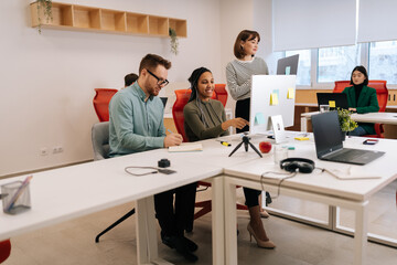 Fototapeta premium Busy multiethnic startup business team brainstorming using computer at workplace. African and Caucasian coworkers group discussing corporate project software in teamwork at office desk.