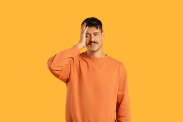 Man with headache on orange studio background