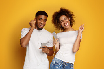 Positive millennial afro man and woman in earphones listening to music