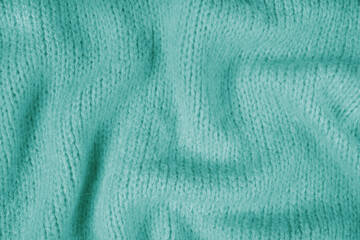 Close up background of turquoise knitted fabric made of viscose yarn. Crumpled knitting wool, soft knitwear texture background. Abstract knitted wrinkled jersey backdrop, wallpaper.