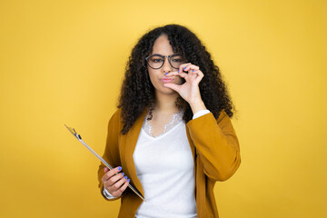 African american business woman with paperwork in hands over yellow background mouth and lips shut...