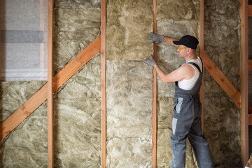 a construction worker insulates the wall of a frame house with mineral wool