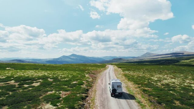 Drone follows 4x4 camper van drive on a gravel mountain road on sunny day with blue skies and clouds. Road trip adventure in overlanding van with solar setup on roof rack. Overland travel 