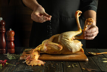 Before roasting, the rooster must be salted. The cook adds salt to raw chicken on the kitchen table.