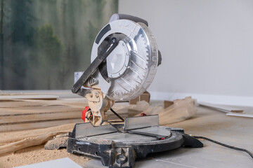 The miter saw or a multi material construction saw on the floor of the apartment with tape measure...