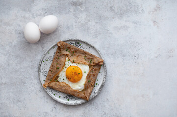Homemade buckwheat crepes. Galettes Bretonnes with cheese and fried egg on a grey background. Traditional French cuisine.