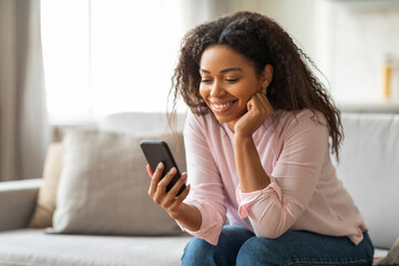 Happy black lady using smartphone at home