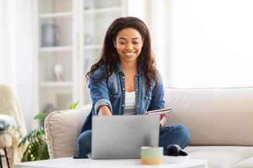 Smiling black lady using laptop at home