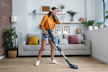 Shot of young happy woman listening and dancing to music while cleaning the living room floor with...