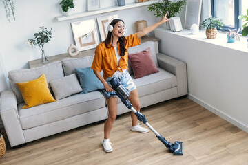Shot of young happy woman listening and dancing to music while cleaning the living room floor with a vaccum cleaner