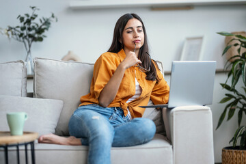 Pretty young woman working with her laptop while sitting on couch at home.