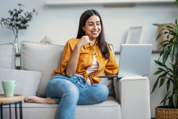 Smiling young woman working with her laptop while sitting on couch at home.