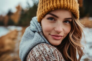 Attractive young woman with beanie smiling in an autumn setting by the lake
