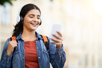 Indian student smiling with headphones, using phone