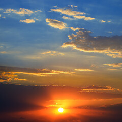 Dramatic sunset background with bright sun, blue sky and clouds.
