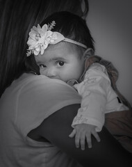 Black and white portrait of African-American baby girl leaning on her mother shoulder and looking at camera