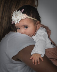 Portrait of African-American baby girl leaning on her mother shoulder and looking at camera
