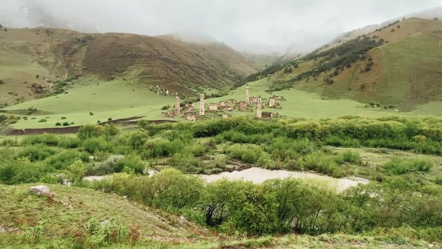 View of the medieval Targim tower complex in the Caucasus mountains surrounded by greenery. The Caucasus Mountains on a cloudy day in Ingushetia. Russia, 4K.