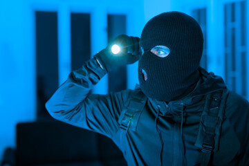 Masked burglar looking around in dark apartment