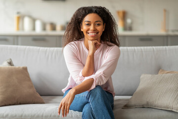 Smiling black lady seated on a sofa at home