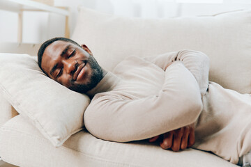 Stressed African American man with a headache sitting alone on a couch in his home He looks tired,...