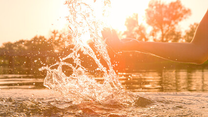 CLOSE UP, LENS FLARE: Female hand splashing water in golden light of setting sun