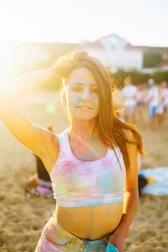 Happy woman covered in rainbow colored powder celebrating holi color festival. Young woman having fun with colorful powder outdoors. Beach party. Traditional Indian holiday.
