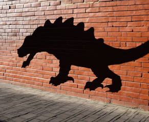 Big black dinosaur shadow on red brick wall outdoors on sunny day. Prehistoric animal silhouette
