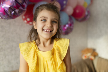 Fototapeta na wymiar Laughing real girl 7 years old in yellow dress against backdrop of festive balloons in holiday at home