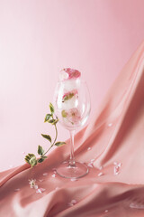Ice cubes with flowers melting in the drink on a silky pink fabric in the background