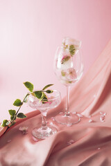 Ice cubes with flowers melting in the drink on a silky pink fabric in the background