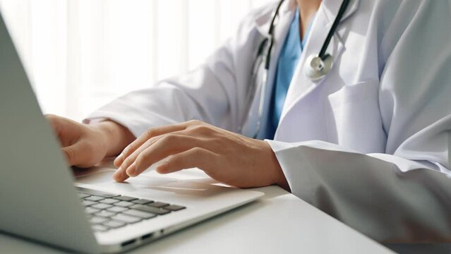 Doctor at hospital sit at his desk working on laptop diagnosing patient test results, developing treatment plan for illnesses and sicknesses. Medical staff and healthcare service. Slow motion. Rigid.